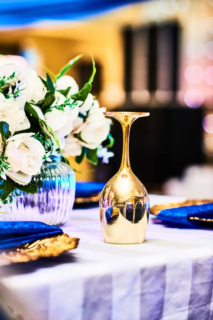 Table de cérémonie : bouquet de fleurs blanches, verre doré et serviette bleue sur nappe blanche