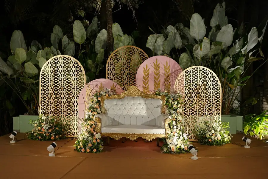 Espace des mariés : banquette capitonnée entre des arches dorées ajourées et des compositions florales