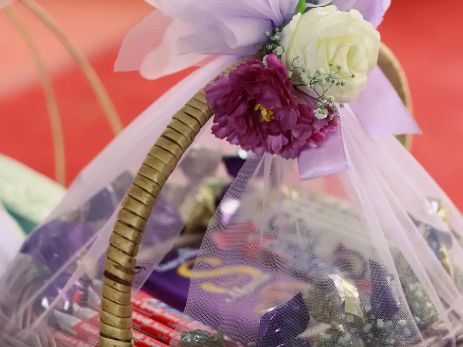 Panier tressé garni de cadeaux emballés et décoré de fleurs et d'un nœud de tulle