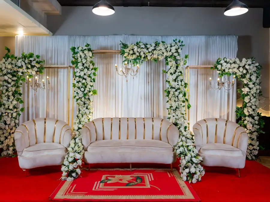 Estrade de mariage : banquettes blanches encadrées de colonnes de fleurs blanches sur tapis rouge